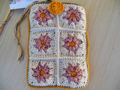 crochet kindle sleeve on the reverse side lay flat with button for keeping it secure the back is made up of small crochet squares in natural with pink flowers.