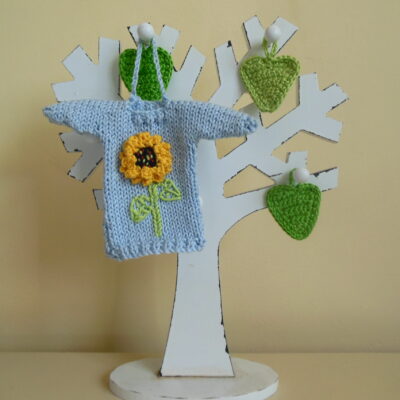 Hand knit minature jumper ornament in blue with a bright yellow sunflower applique hanging on a wooden tree photo prop