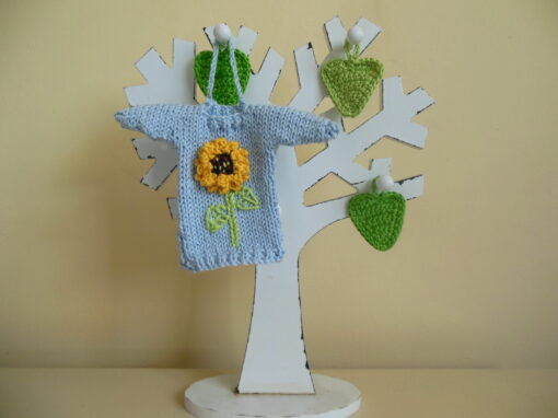 Hand knit minature jumper ornament in blue with a bright yellow sunflower applique hanging on a wooden tree photo prop