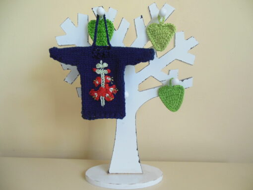 Hand knit minature jumper ornament in navy blue with an embroidered gladioli flower design hanging on a wooden tree photo prop.