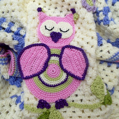 Crochet baby blanket close up cream with a vibrant pink owl on a leafy branch design the owl has a cute little heart shaped beak.