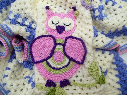 Crochet baby blanket close up cream with a vibrant pink owl on a leafy branch design the owl has a cute little heart shaped beak.