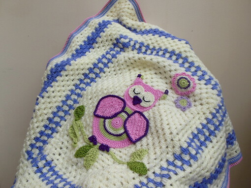 Crochet baby blanket draped over a chair showing the owl and branch in the centre of the blanket and the surrounding purple and cream borders.